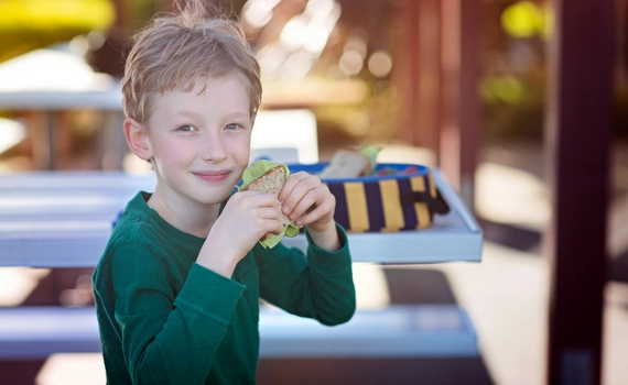 Child holding up his lunch outside and eating